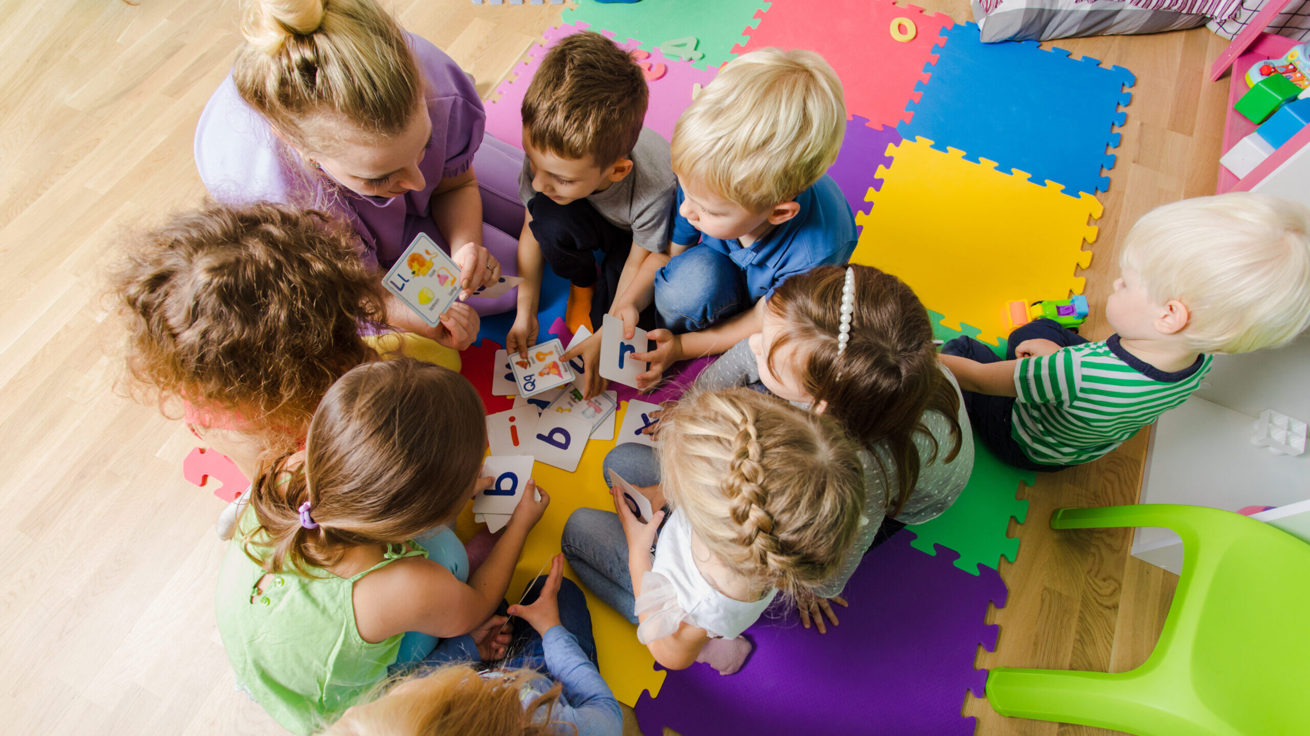 Group of kindergarten kids sitting closely on a floor together with teacher, providing group work. Children learning to cooperate while solving tasks.