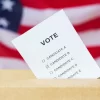 voting and civil rights concept - vote inserted into ballot box slot on election over american flag