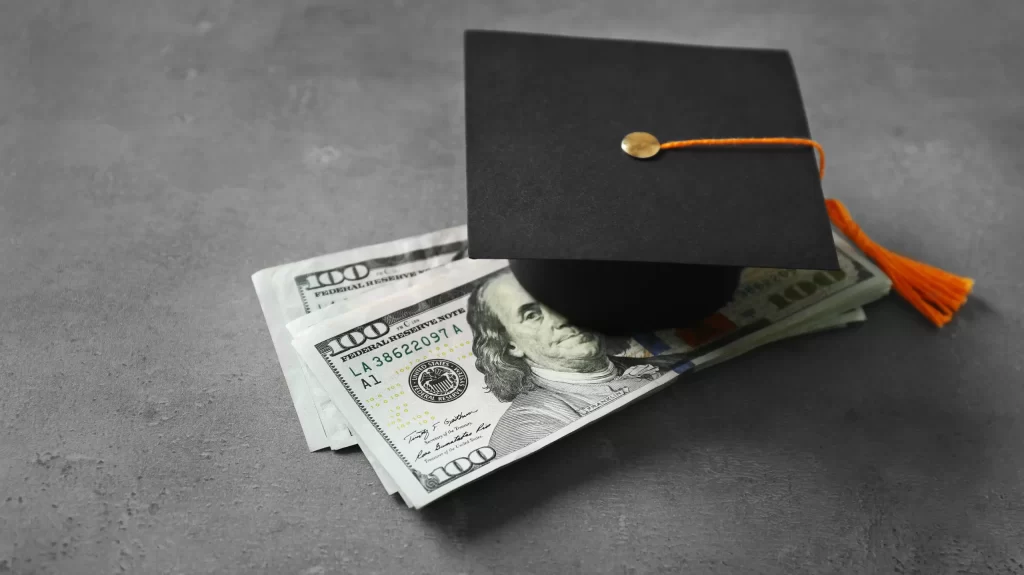 Graduation hat and dollar banknotes on table. Tuition fees concept
