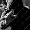 Young unidentifiable teenage boy holding the wired garden at the correctional institute in black and white, conceptual image of juvenile delinquency, focus on the boys hand.