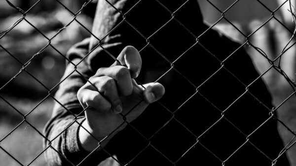Young unidentifiable teenage boy holding the wired garden at the correctional institute in black and white, conceptual image of juvenile delinquency, focus on the boys hand.
