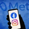 Illustration of a silhouetted hand holding a smartphone displaying Facebook and Instagram logos beneath the Meta logo.